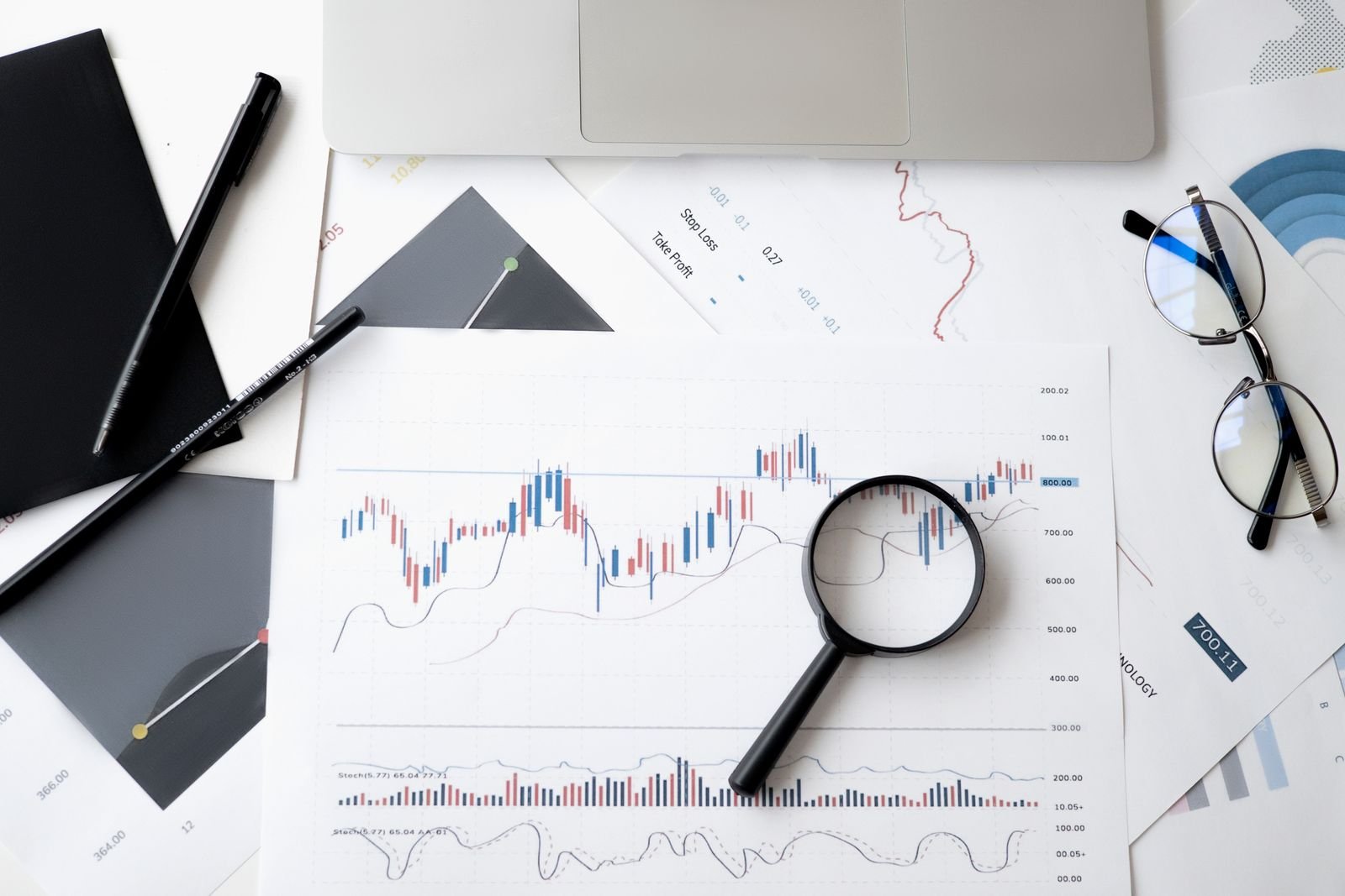 Relatórios impressos com gráficos de desempenho, lupa, óculos e notebook sobre mesa de trabalho