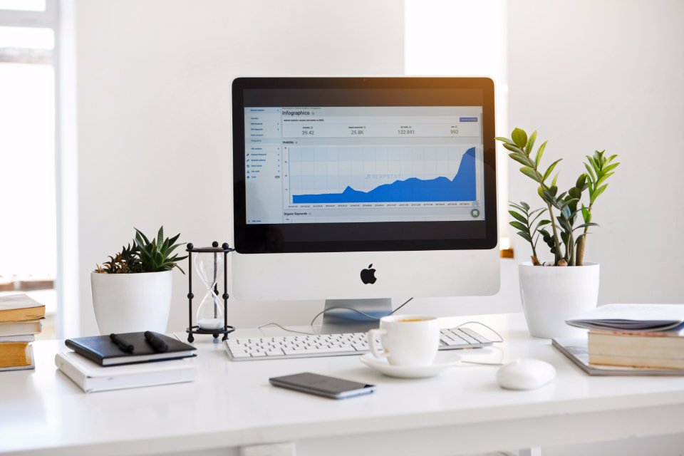 Mesa de trabalho com monitor exibindo painel de métricas e gráficos de desempenho de campanha